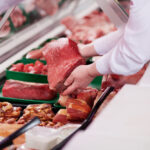 Saleswoman,Offering,Fresh,Meat,At,Display,In,Supermarket